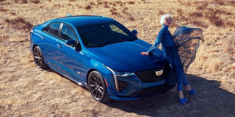 Blue Cadillac CT4-V parked on the desert while a woman in a blue dress sits on the hood