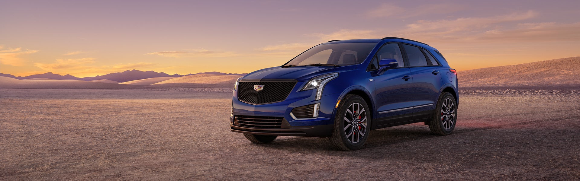 Blue Cadillac XT5 parked in the desert while it is turning dusk outside