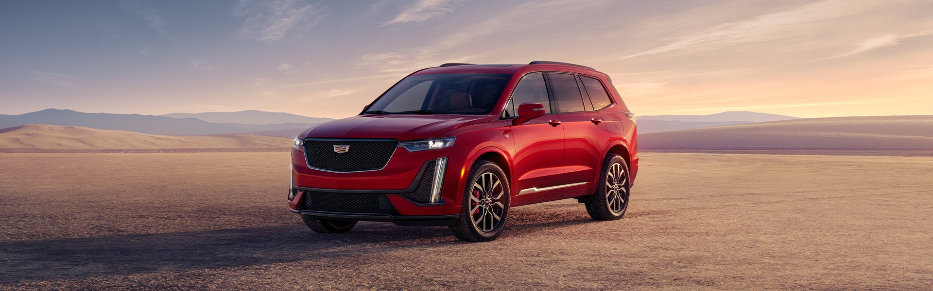 Red Cadillac XT6 parked on the desert while dusk is setting in